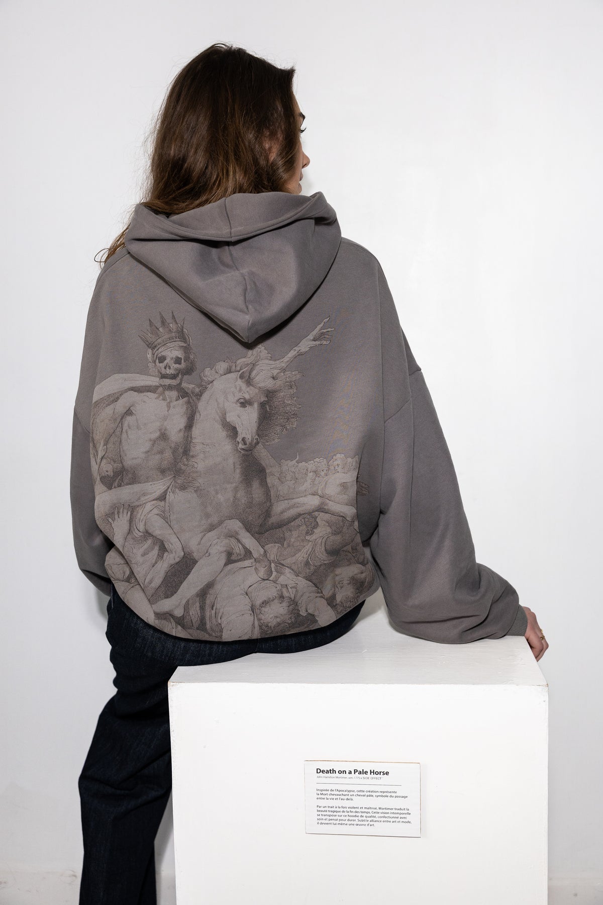 Hoodie gris porté de dos, assise sur un socle d'exposition